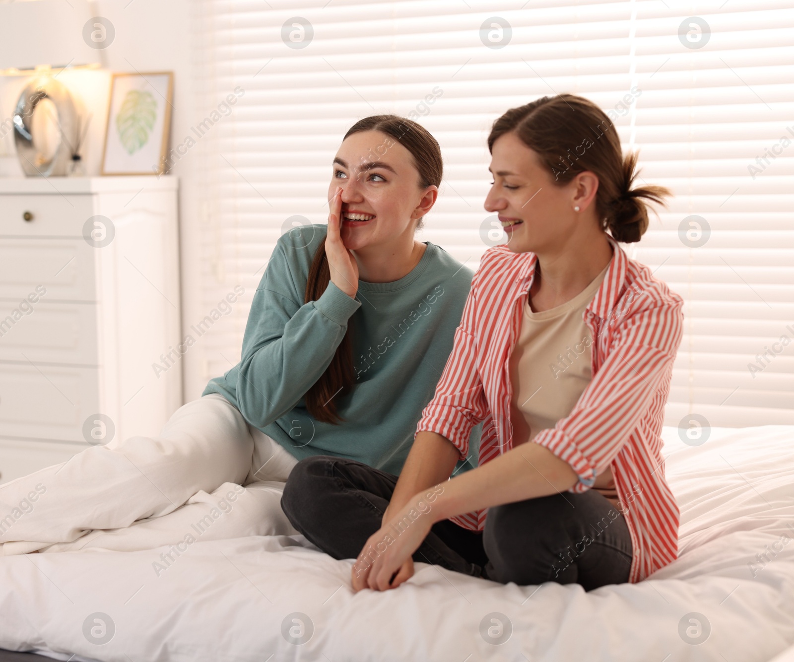 Photo of Woman talking to her friend and laughing on bed at home