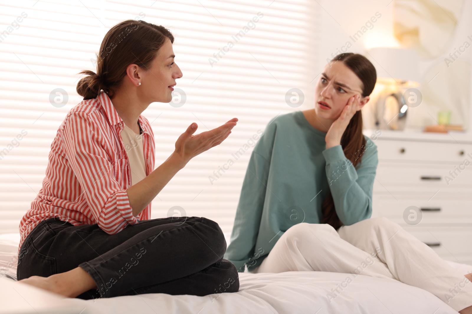 Worried woman listening to her friend on bed at home Photo of Worried woman listening to her friend on bed at home