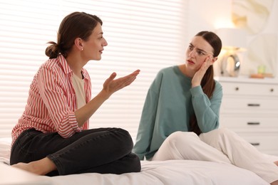 Photo of Worried woman listening to her friend on bed at home