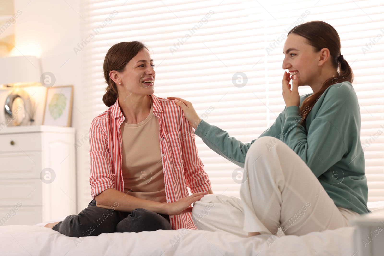 Photo of Woman talking to her friend and laughing on bed at home