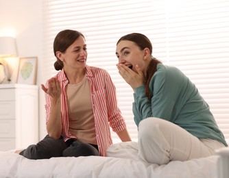 Photo of Woman talking to her friend and laughing on bed at home