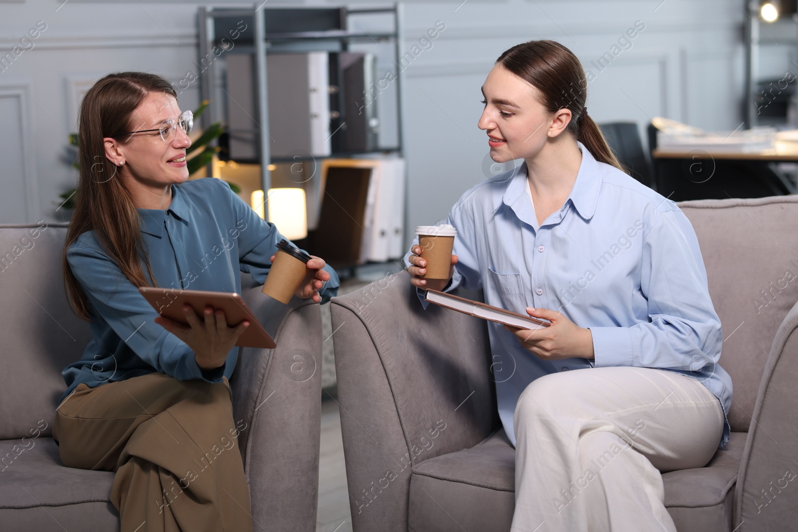 Photo of Coworkers with tablet. notebook and coffee discussing project in office