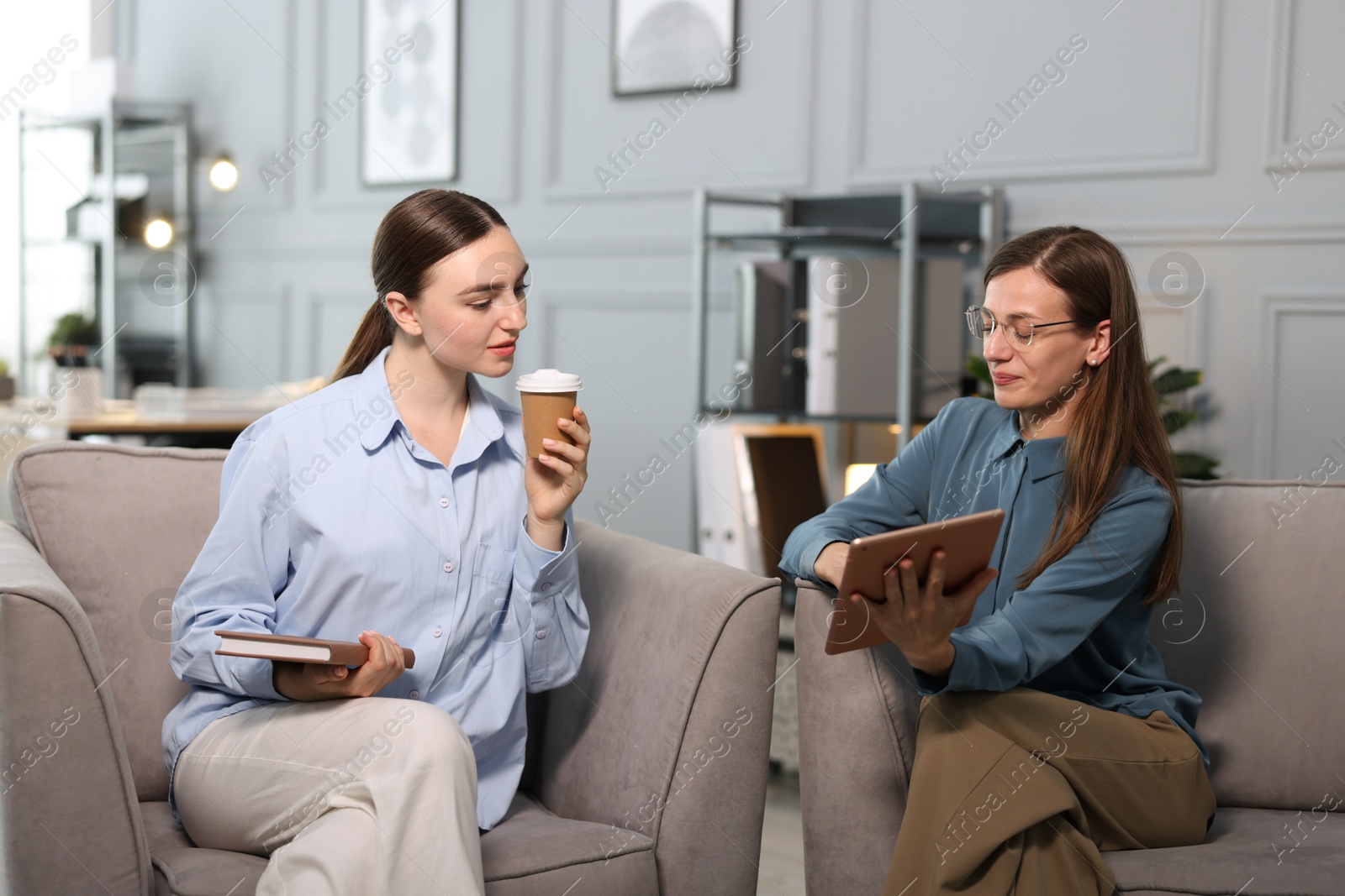 Photo of Coworkers with tablet. notebook and coffee discussing project in office