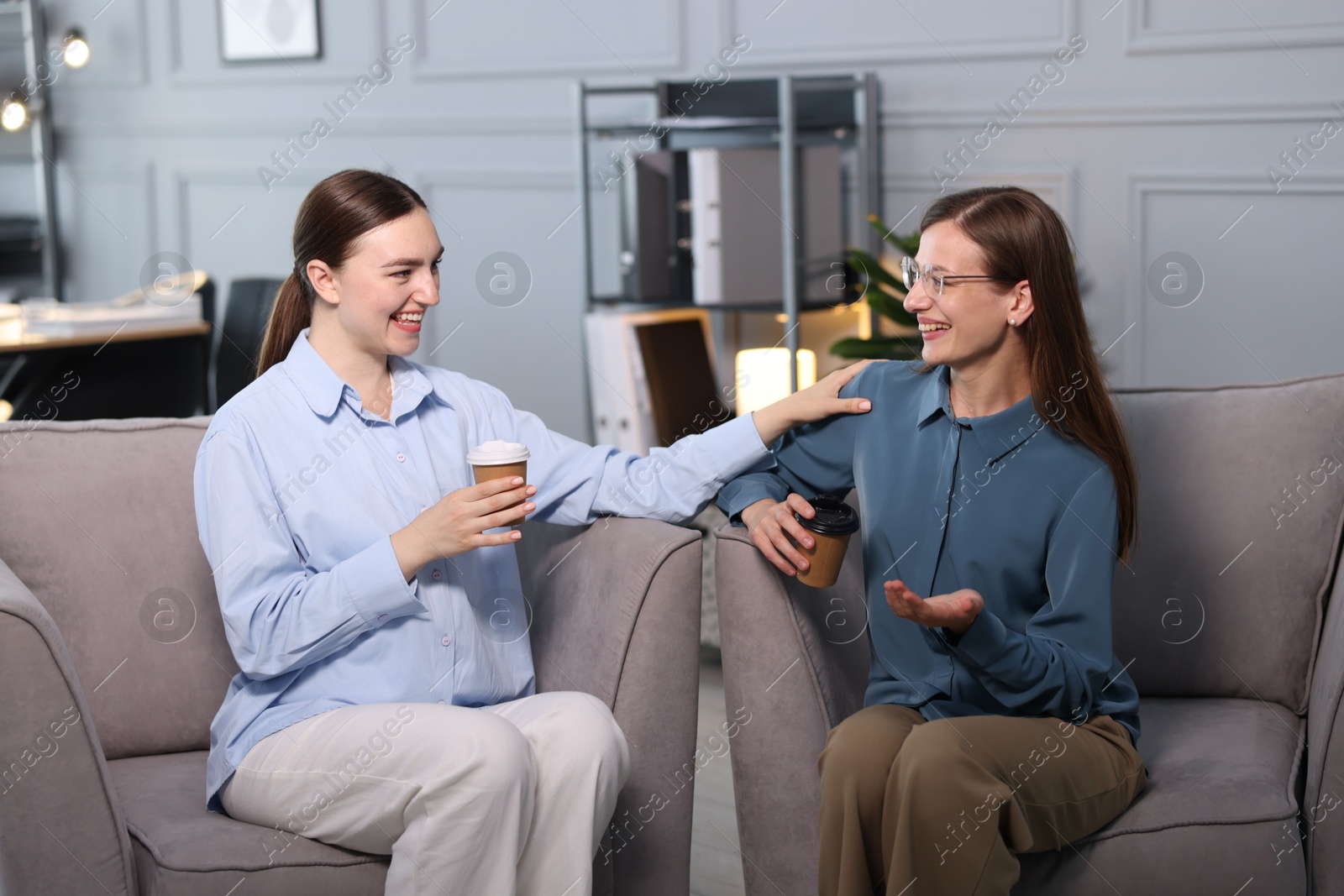 Photo of Coworkers talking during coffee break in armchairs at office