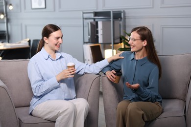 Photo of Coworkers talking during coffee break in armchairs at office