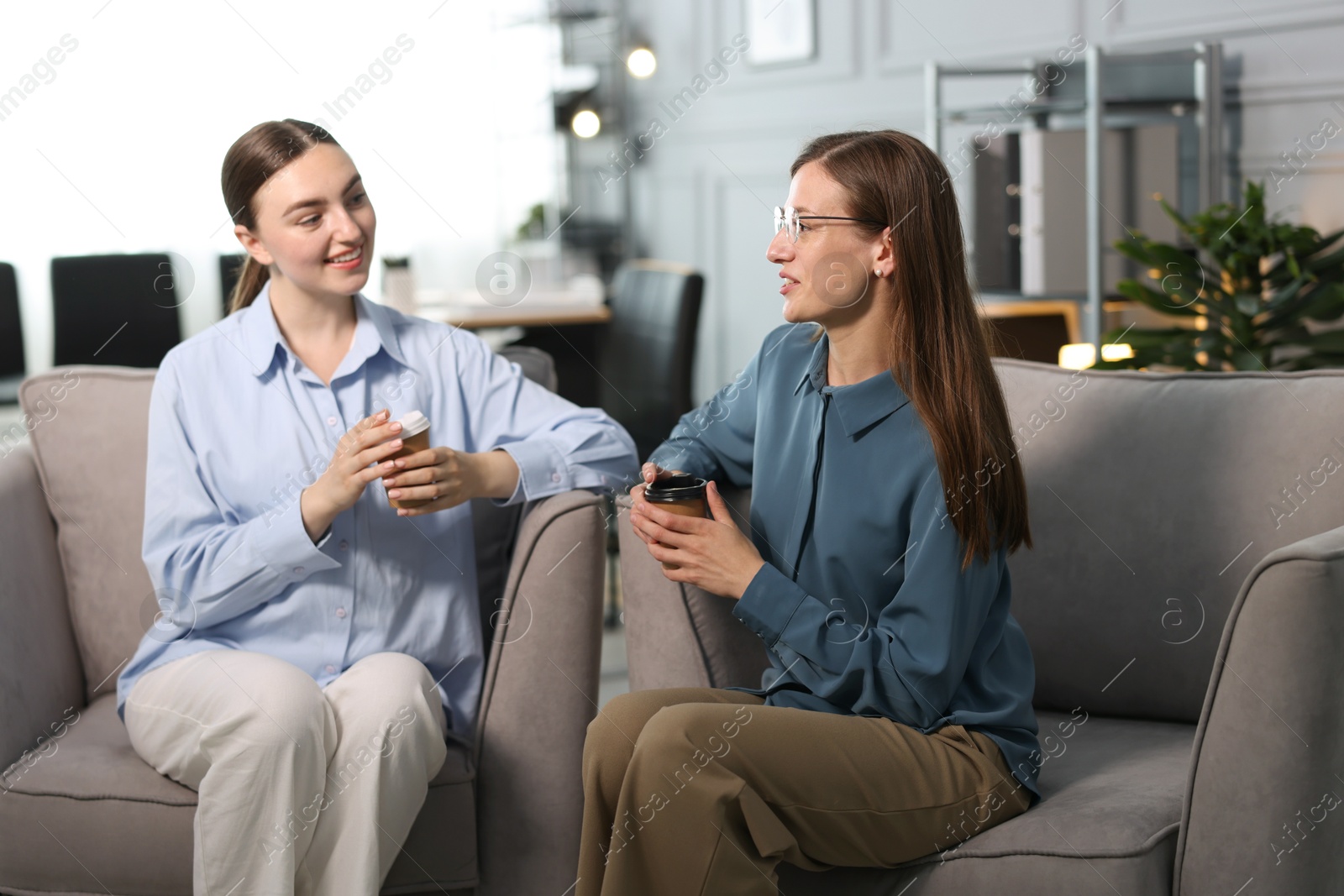 Coworkers talking during coffee break in armchairs at office Photo of Coworkers talking during coffee break in armchairs at office