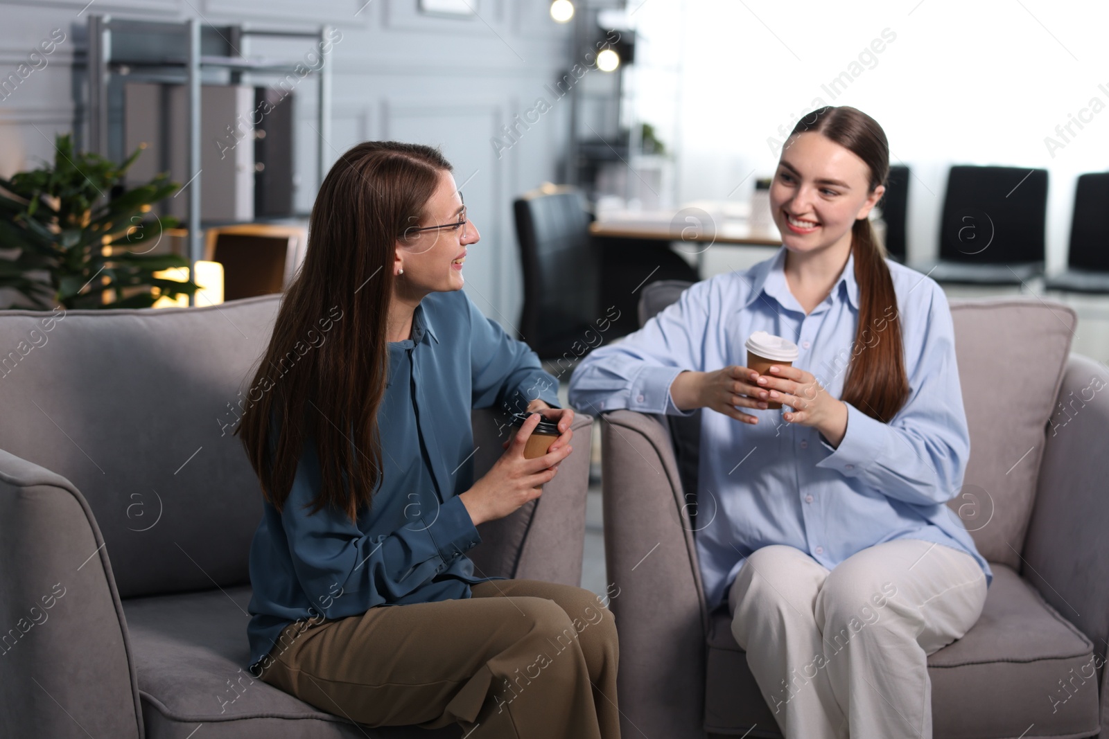 Coworkers talking during coffee break in armchairs at office Photo of Coworkers talking during coffee break in armchairs at office