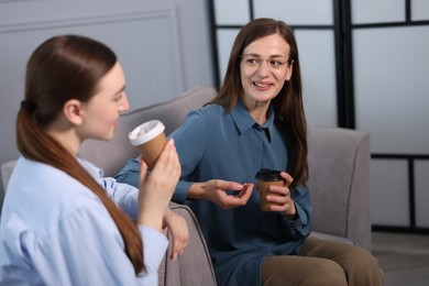 Photo of Coworkers talking during coffee break in armchairs at office