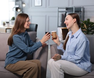 Photo of Coworkers talking during coffee break in armchairs at office