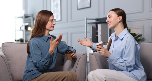 Photo of Coworkers talking during coffee break in armchairs at office