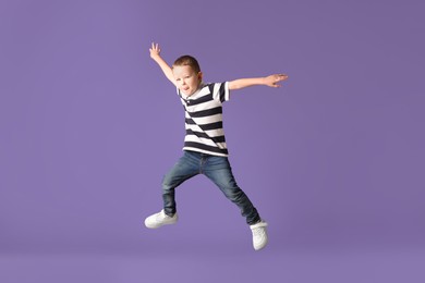 Photo of Cute little boy jumping on purple background