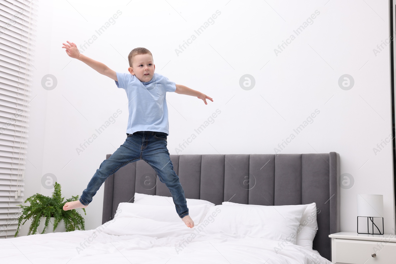 Cute little boy jumping on bed at home, space for text Photo of Cute little boy jumping on bed at home, space for text
