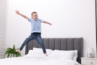 Photo of Cute little boy jumping on bed at home, space for text