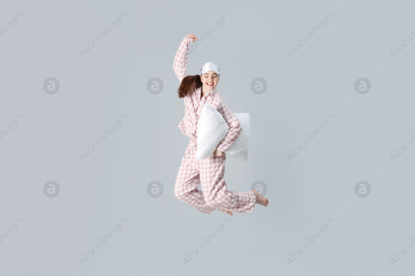 Woman in pyjama with pillow jumping on grey background Photo of Woman in pyjama with pillow jumping on grey background