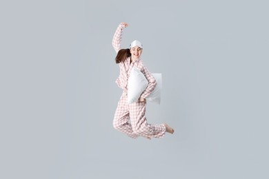 Photo of Woman in pyjama with pillow jumping on grey background
