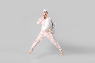 Photo of Woman in pyjama with pillow jumping on grey background