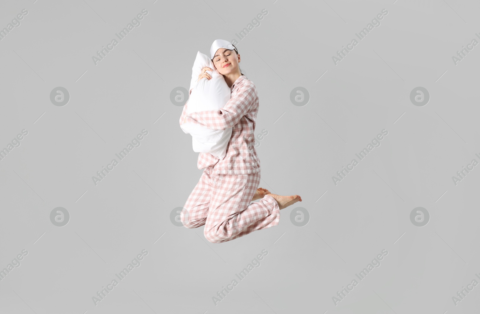Woman in pyjama with pillow jumping on grey background Photo of Woman in pyjama with pillow jumping on grey background
