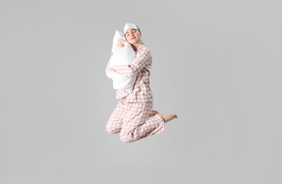 Photo of Woman in pyjama with pillow jumping on grey background