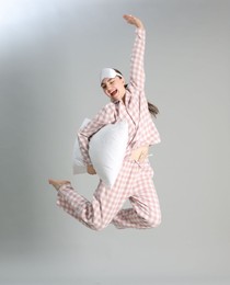 Photo of Woman in pyjama with pillow jumping on grey background