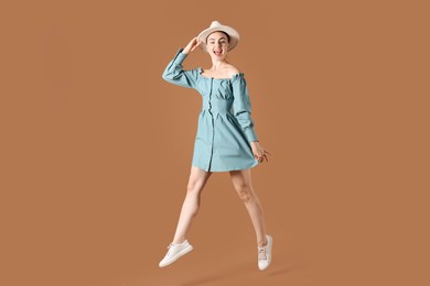 Photo of Woman in stylish hat jumping on brown background