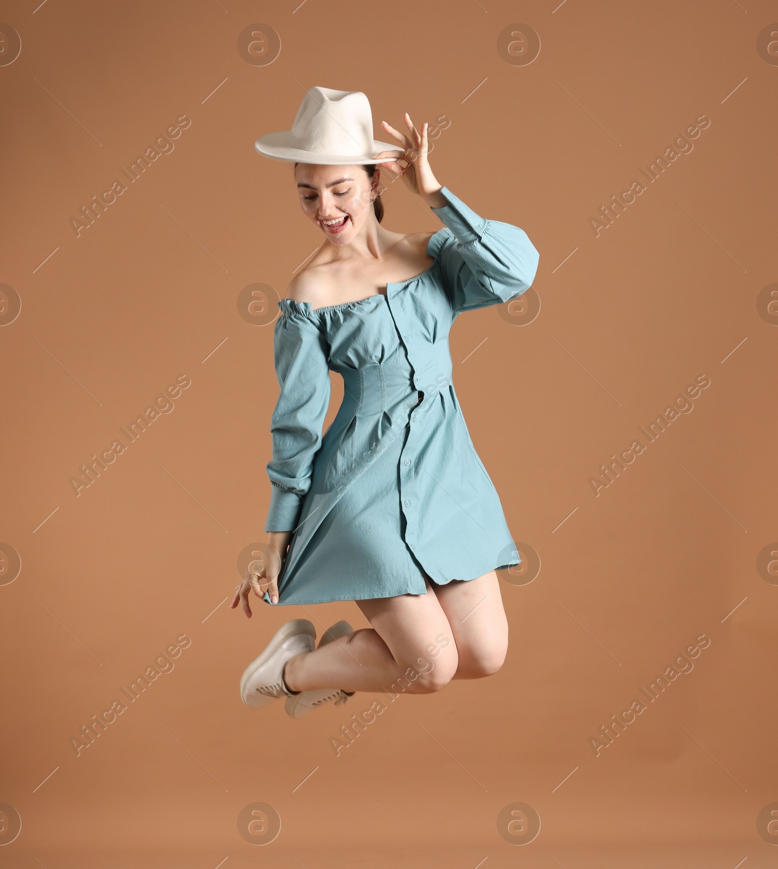 Woman in stylish hat jumping on brown background Photo of Woman in stylish hat jumping on brown background