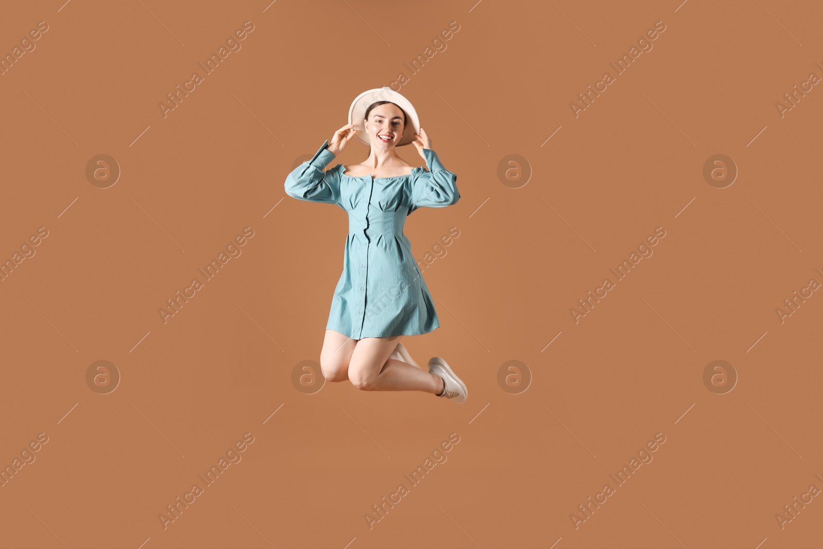 Woman in stylish hat jumping on brown background Photo of Woman in stylish hat jumping on brown background