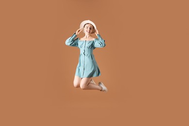 Photo of Woman in stylish hat jumping on brown background