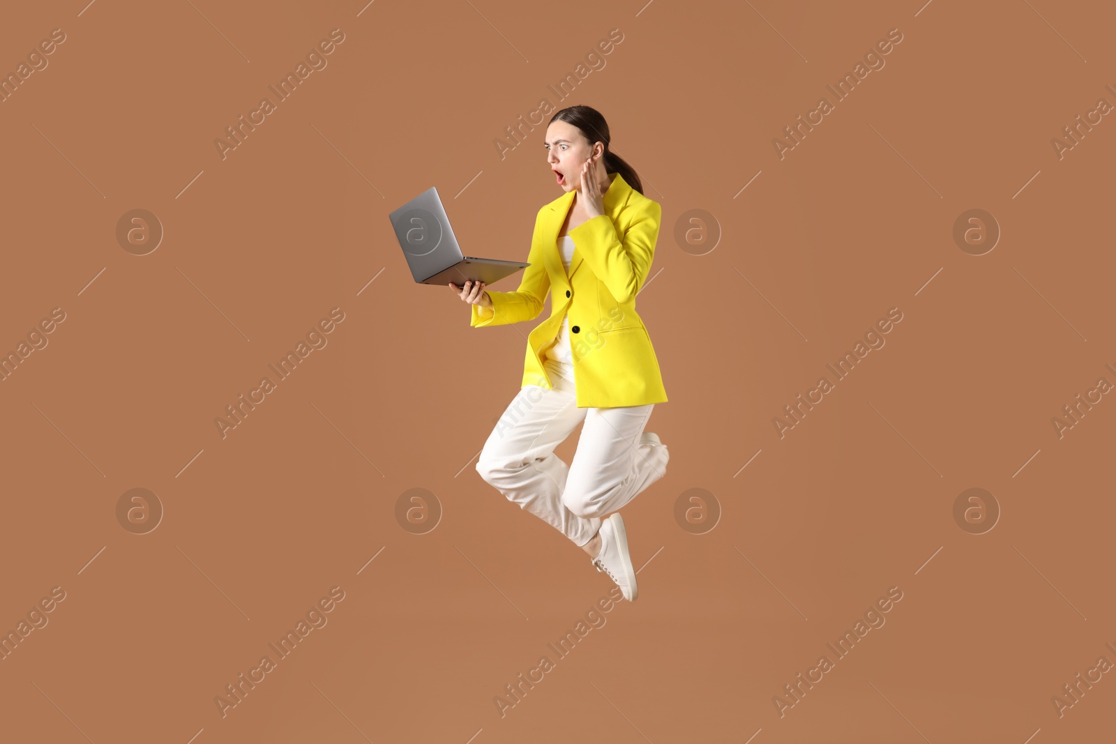 Woman with laptop jumping on brown background Photo of Woman with laptop jumping on brown background