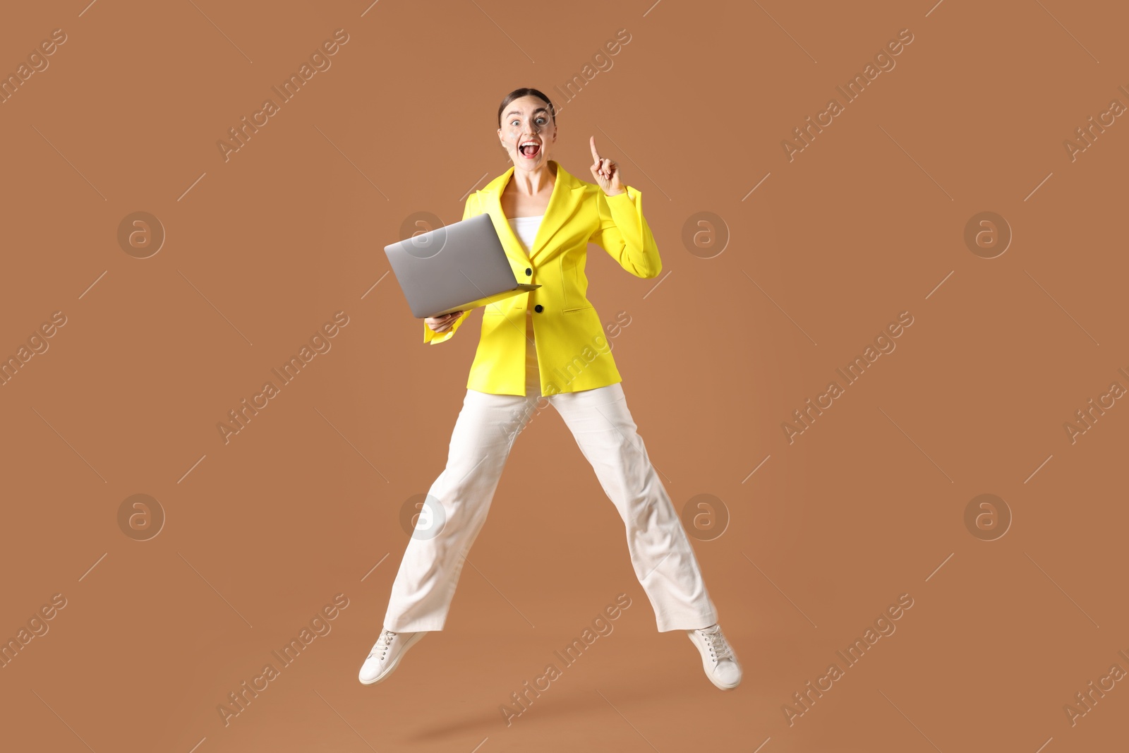 Woman with laptop jumping on brown background Photo of Woman with laptop jumping on brown background