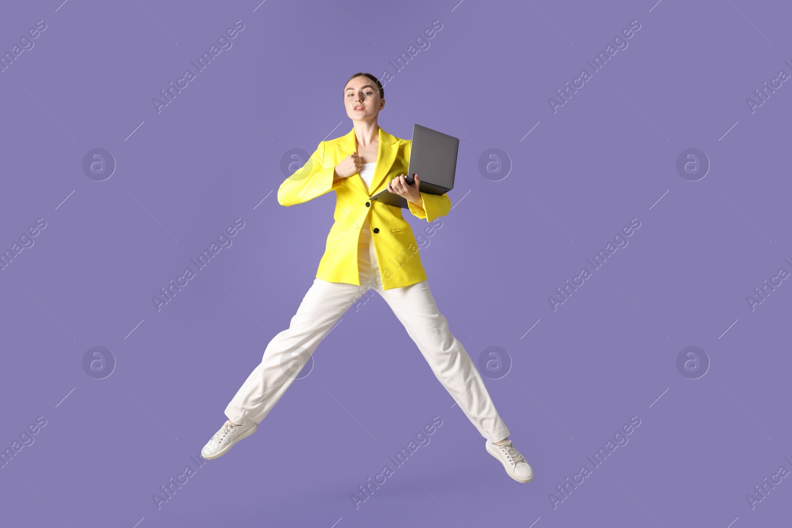 Woman with laptop jumping on purple background Photo of Woman with laptop jumping on purple background