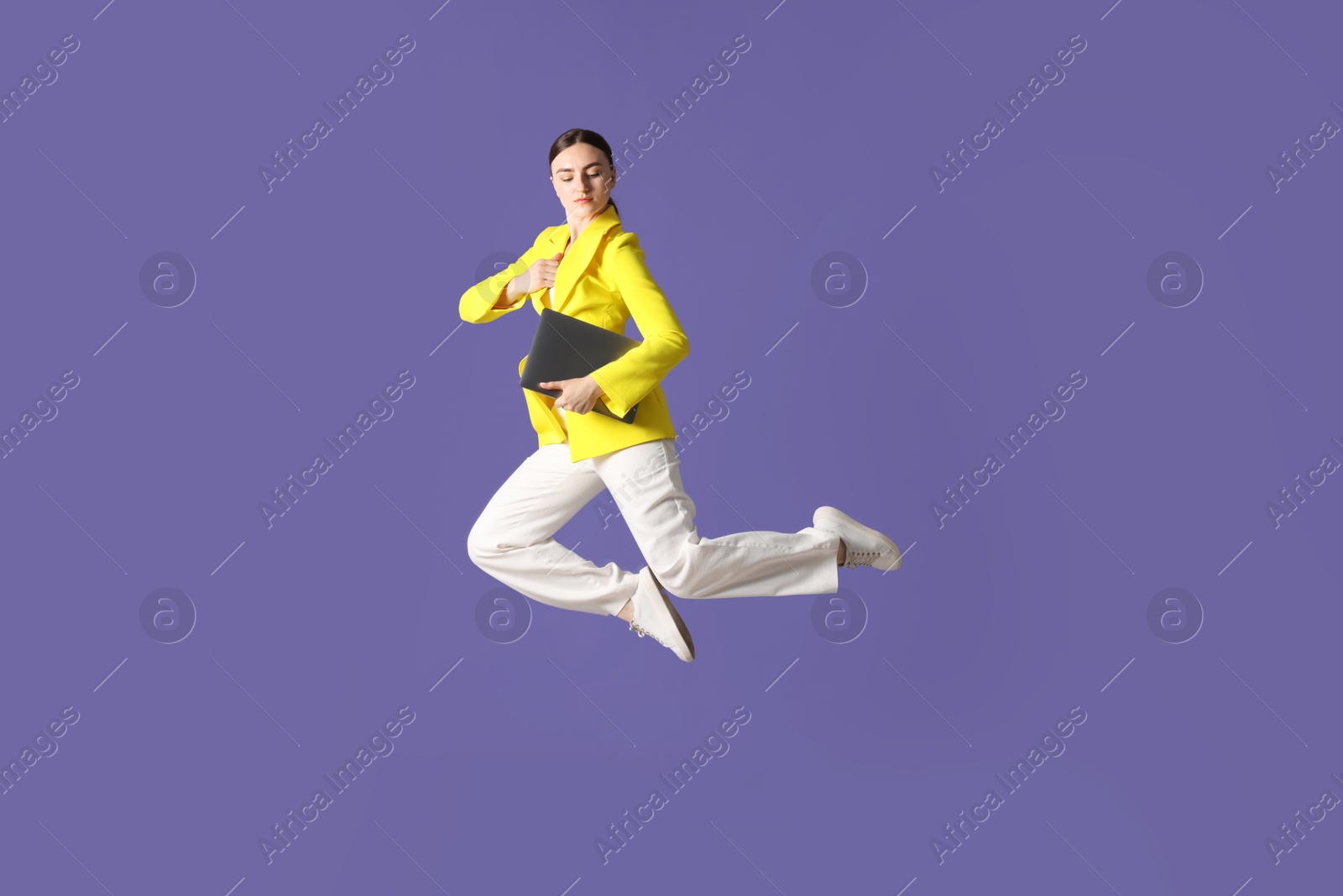 Woman with laptop jumping on purple background Photo of Woman with laptop jumping on purple background