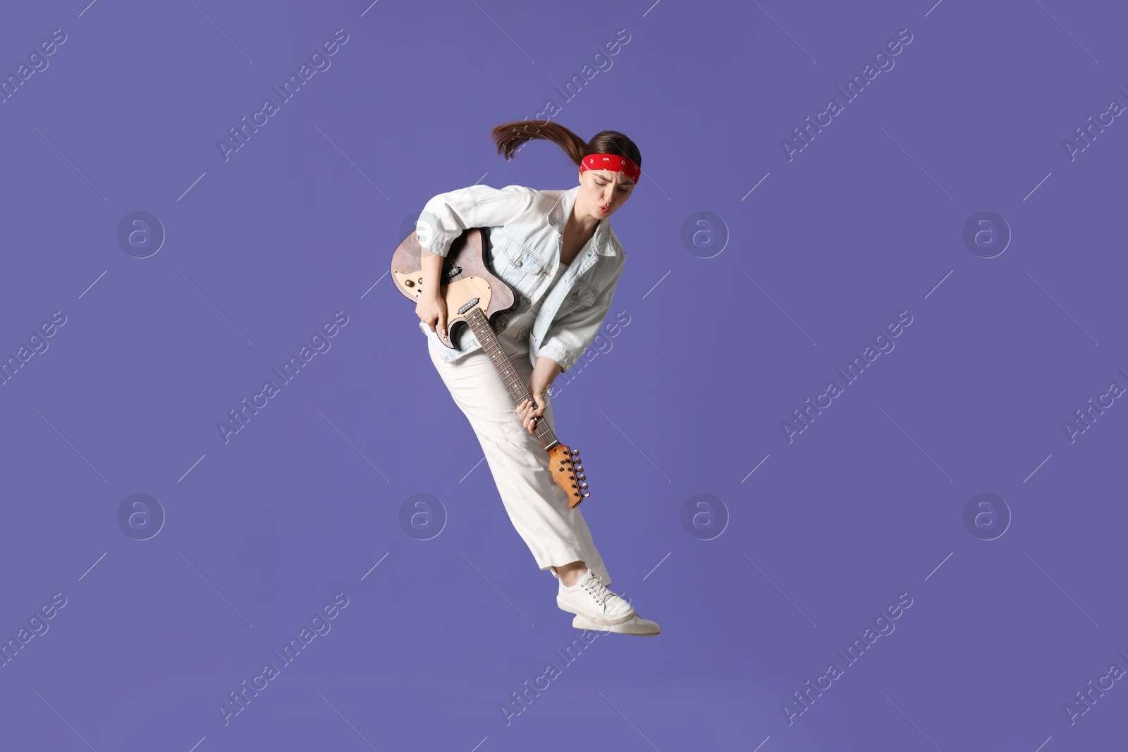 Woman with guitar jumping on purple background Photo of Woman with guitar jumping on purple background