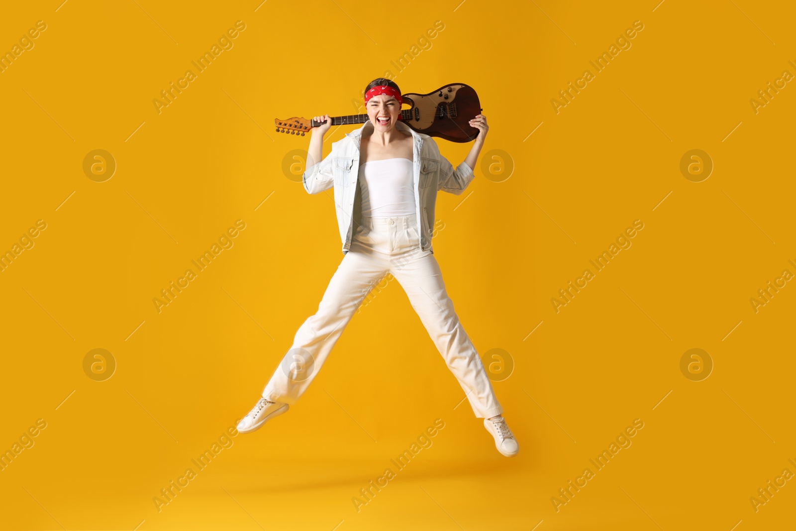 Woman with guitar jumping on orange background Photo of Woman with guitar jumping on orange background