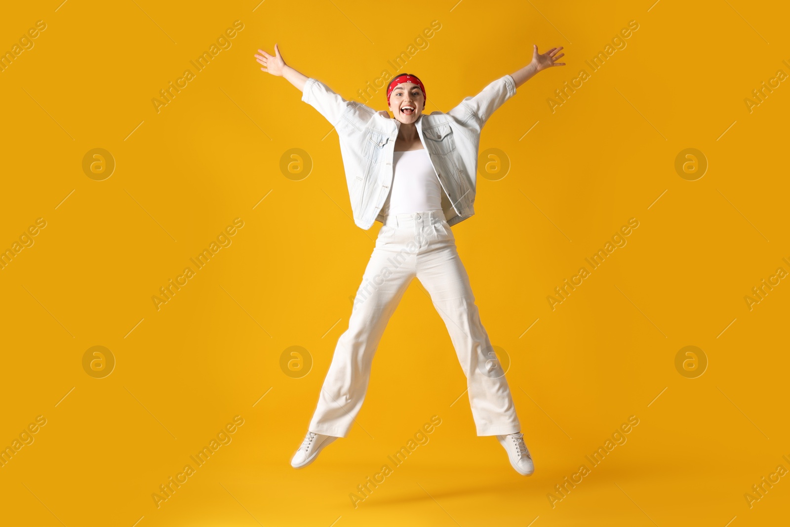 Woman in stylish outfit jumping on orange background Photo of Woman in stylish outfit jumping on orange background
