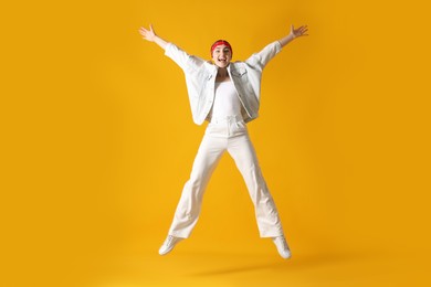 Photo of Woman in stylish outfit jumping on orange background