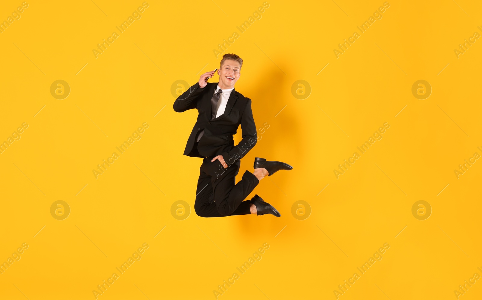 Businessman jumping while talking on smartphone against orange background Photo of Businessman jumping while talking on smartphone against orange background