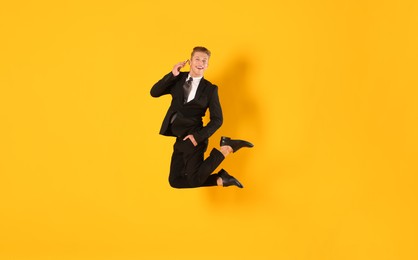 Photo of Businessman jumping while talking on smartphone against orange background
