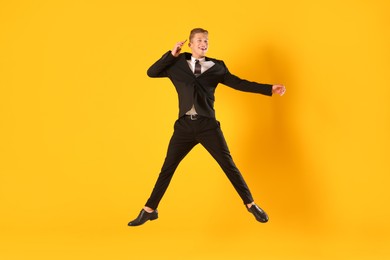 Photo of Businessman jumping while talking on smartphone against orange background