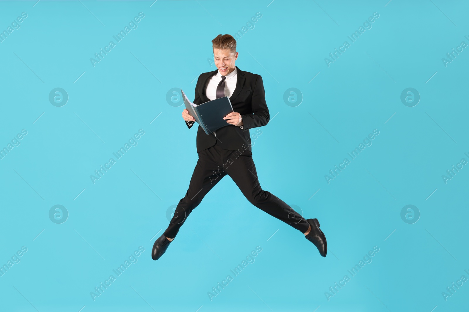 Businessman with folder jumping on light blue background Photo of Businessman with folder jumping on light blue background