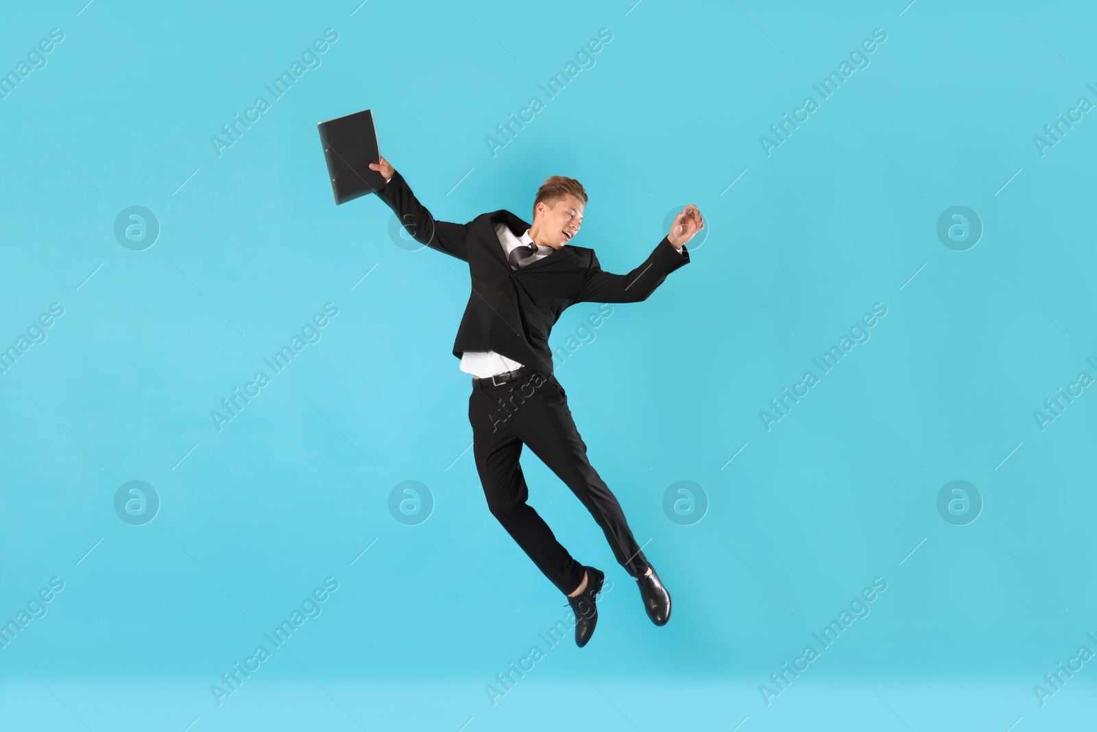 Businessman with folder jumping on light blue background Photo of Businessman with folder jumping on light blue background
