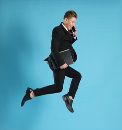Photo of Businessman with folder jumping while talking on smartphone against light blue background