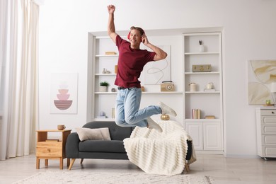 Photo of Happy man jumping while listening to music at home