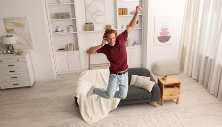 Photo of Happy man jumping while listening to music at home