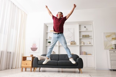 Photo of Happy man jumping while listening to music at home, low angle view