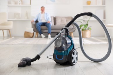 Photo of Man resting on sofa at home, focus on vacuum cleaner