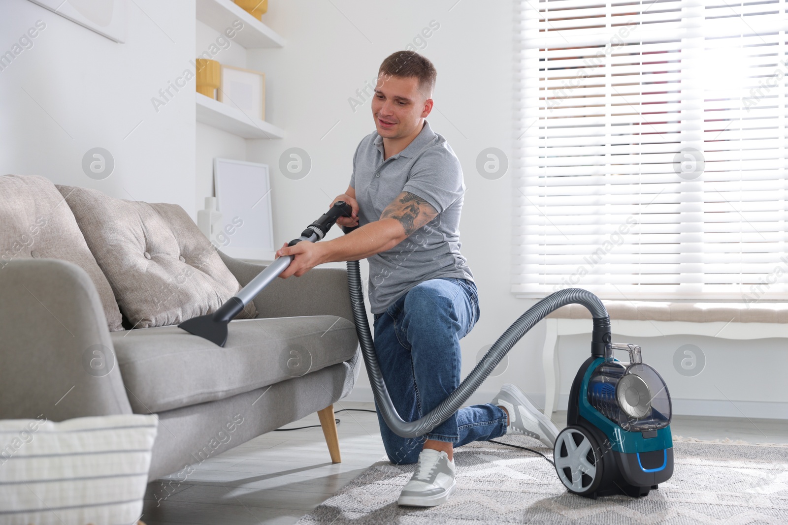 Man cleaning sofa with vacuum cleaner at home Photo of Man cleaning sofa with vacuum cleaner at home