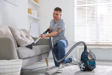 Photo of Man cleaning sofa with vacuum cleaner at home