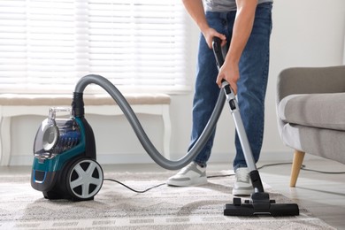 Photo of Man cleaning carpet with vacuum cleaner at home, closeup