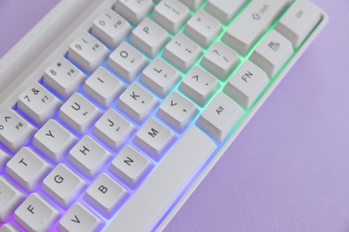 Photo of Modern computer keyboard with RGB lighting on violet background, above view