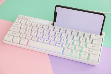 Photo of Modern computer keyboard with RGB lighting and smartphone on color background, closeup